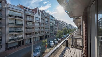 Un immeuble d’habitation doté de nombreux balcons, donnant sur la rue, avec des voitures garées devant.
