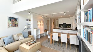 Ein modernes Wohnzimmer mit einer Couch, einem Couchtisch und einem Essbereich mit Stühlen und einem Tisch. Es gibt eine Küchenzeile mit Schränken und einer Arbeitsfläche.