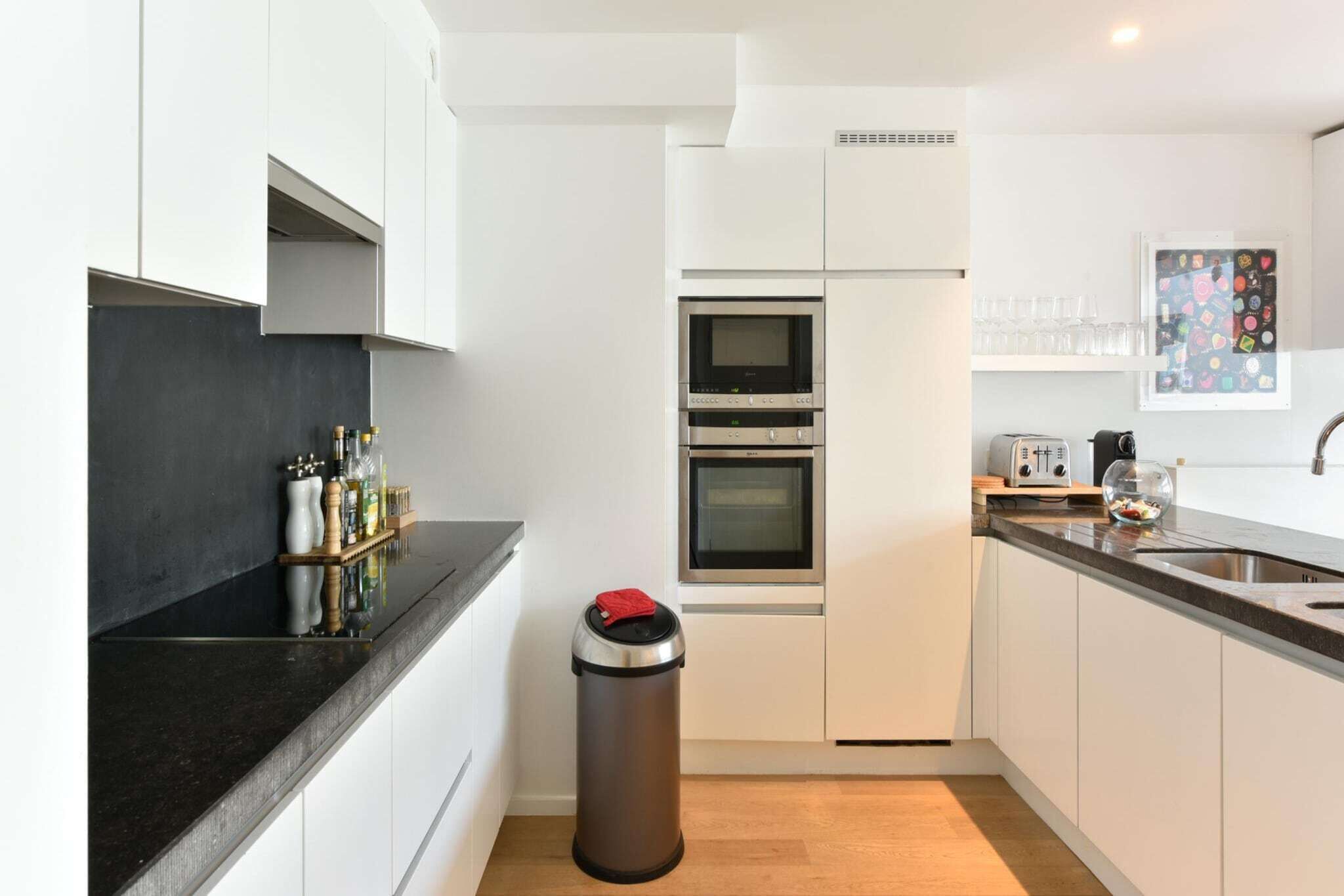 A modern kitchen with white cabinets, a black countertop, a stainless steel trash bin, and a toaster.
