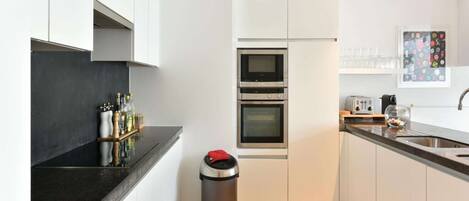 A modern kitchen with white cabinets, a black countertop, a stainless steel trash bin, and a toaster.