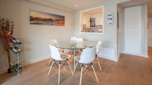 A modern dining area with a glass table, white chairs, and a wine rack. - Apartment in Duinbergen near Sailing School (KNOKKE-HEIST)