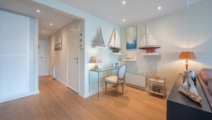 A modern room with a glass table, a chair, and a small shelf with decorative items. - Apartment in Duinbergen near Sailing School (KNOKKE-HEIST)