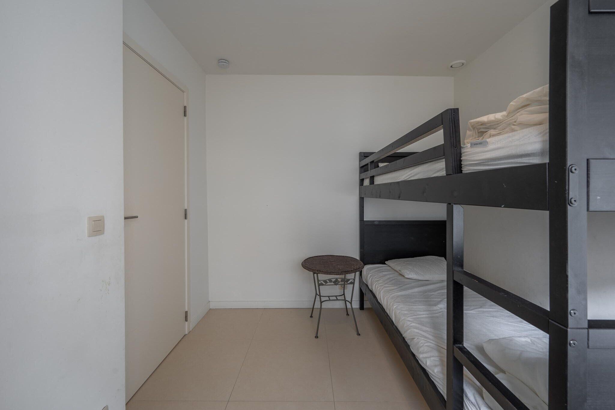 Een studentenkamer met stapelbedden, een klein rond tafeltje en een deur.