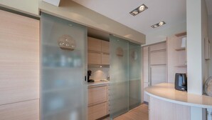 A modern kitchen with light wood cabinetry, a glass partition, and a built-in coffee station. - Apartment in Knokke near the Beach (KNOKKE-HEIST)