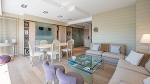 A modern living room with a glass coffee table, beige sofa, and white chairs. - Apartment in Knokke near the Beach (KNOKKE-HEIST)