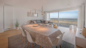 A modern dining area with a large table, chairs, and a view of the ocean through large windows. - Apartment in Knokke with Sea View (KNOKKE-HEIST)
