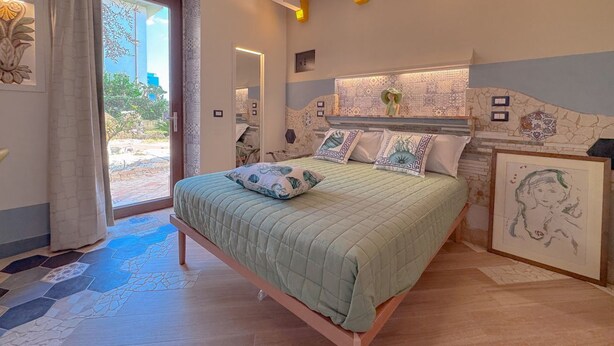 A bedroom with a bed, a door to an outdoor area, and a wall with decorative tiles.