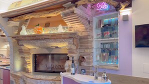 A stone fireplace with a neon sign, a bar area with a counter, and a shelf with glassware.
