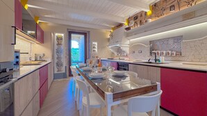 A modern kitchen with a long island, white chairs, and a red accent wall.