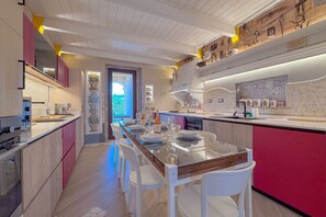 Une cuisine moderne avec un grand îlot central, des chaises blanches et un mur d’accent rouge.