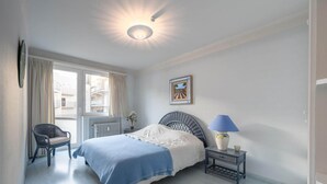 A bedroom with a bed, a chair, a nightstand, a lamp, a window, and a picture on the wall. - Apartment in Knokke near Casino and Beach (KNOKKE-HEIST)