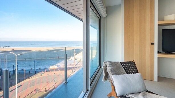A modern room with a large window overlooking a beach, a flat-screen TV, and a cozy seating area.