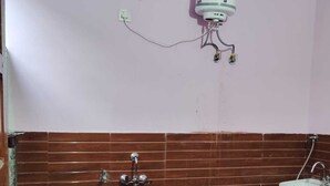 A bathroom with a white sink, a blue bucket, and a water heater mounted on the wall. - Ramakantam Home Stay (Faizabad)