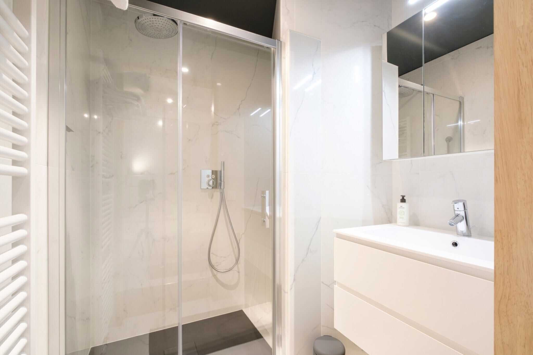 Un baño moderno con ducha de vidrio, un lavamanos blanco y un espejo encima.