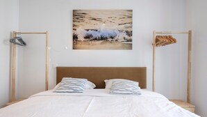 Ein Schlafzimmer mit einem hölzernen Kopfteil, zwei Kissen, einer weißen Bettdecke und einem Gemälde mit einer Strandansicht an der Wand.