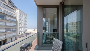 Ein Balkon mit Blick auf eine Straße und Gebäude, ein Stuhl und eine Glastür.