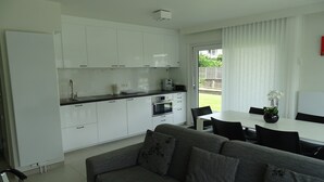 Una cocina moderna con armarios blancos, un comedor con mesa y sillas, y un sofá gris.