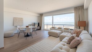 A modern living room with a large window, a dining area, and a sofa with decorative pillows.