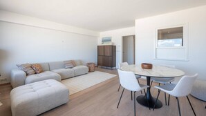 A modern living room with a sofa set, ottoman, dining table with chairs, and a cabinet.