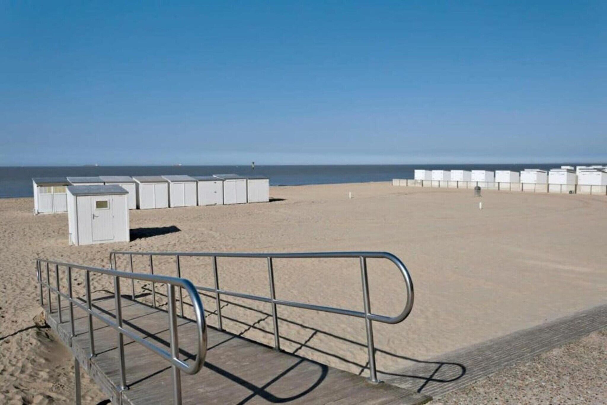 Una playa con cabañas de playa blancas y una barandilla de metal.