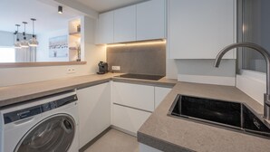 Une cuisine moderne avec des meubles blancs, un lave-linge encastré, une machine à café et un évier en acier inoxydable.