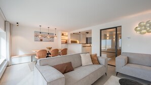 Un salon moderne avec un canapé, un coin repas avec des chaises et une cuisine en arrière-plan.