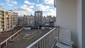 Vista da un balcone su un cortile con diversi edifici, una sedia bianca e cielo sereno.