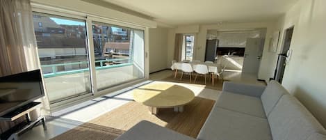 Una sala moderna con sofá, televisión y un comedor con mesa y sillas.
