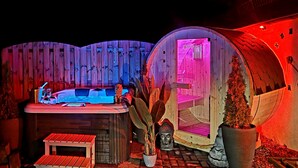 A hot tub and two wooden domes with neon lighting, surrounded by plants and a wooden fence. - Ferienhaus Mefady Jünkerath (Jünkerath)