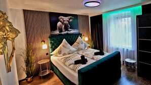 A modern bedroom with a green upholstered bed, a large elephant artwork above the bed, and a small round table by the window. - Ferienhaus Mefady Jünkerath (Jünkerath)