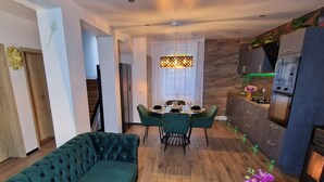 A modern living room with a green sofa, a dining table with chairs, and a kitchen area with appliances. - Ferienhaus Mefady Jünkerath (Jünkerath)