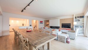 Ein modernes Wohnzimmer mit Esstisch aus Holz, einer Couch, einem Fernseher und einem Bücherregal.