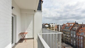 Un balcon avec une balustrade blanche, une petite table et une vue sur les immeubles voisins.
