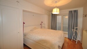 Un dormitorio con cama, ventana con cortinas, radiador y lámpara colgante.