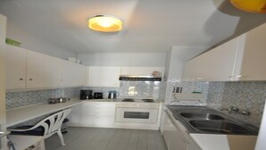 A compact kitchen with white cabinets, a stove, a sink, and a chair. - Studio in Knokke-Heist near the Beach (KNOKKE-HEIST)