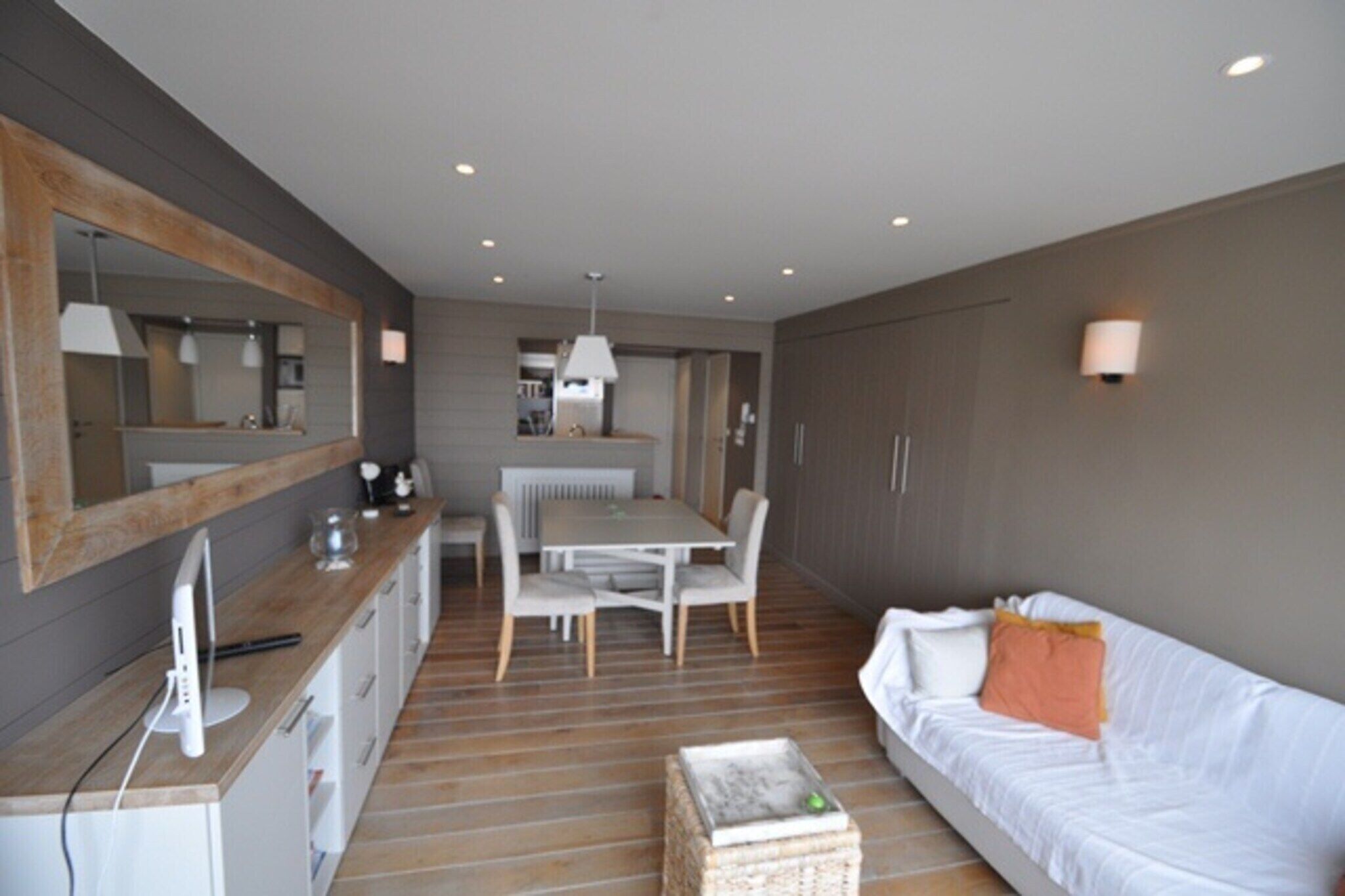 Une chambre d’hôtel moderne avec un plancher en bois, un canapé blanc, une table à manger avec des chaises, un coin cuisine et un grand miroir.