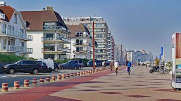 Een kustpromenade met moderne gebouwen, een fietspad en geparkeerde auto's.