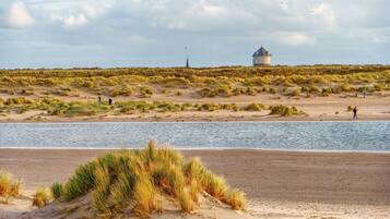 Een strand met duinen, een waterpartij en een gebouw in de verte.