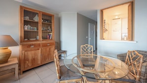 Un comedor con mesa de vidrio y sillas de mimbre, un mueble de madera con puertas de cristal y un sofá a cuadros.