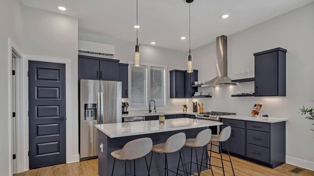 Una cocina moderna con una isla central, taburetes de bar y un refrigerador de acero inoxidable.