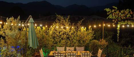 An outdoor seating area with tables and chairs, surrounded by potted plants and string lights.
