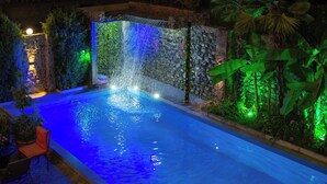 A swimming pool with a waterfall feature, surrounded by greenery and a stone wall. - Hotel and Restaurant VILLA GIVISI (Lagodekhi)