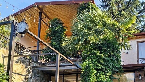 A patio with a hanging chair, potted plants, and a clock. - Hotel and Restaurant VILLA GIVISI (Lagodekhi)