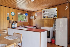 A compact kitchen with wooden walls, a wooden dining table, and a refrigerator. - Charming holiday home in peaceful surroundings (Gedser)
