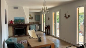 A spacious living area with a fireplace, a dining table, and a kitchen in the background. - Seaside villa, Gulf of LAVA, Appietto, South Corsica (Appietto)