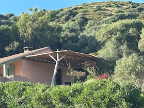 Ein rustikales Haus mit Ziegeldach, umgeben von üppigem Grün und Hügeln im Hintergrund.