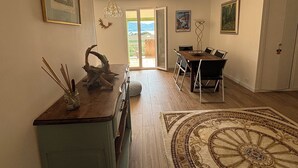 A dining area with a wooden table and chairs, a chandelier, and a view through a glass door to the outside. - Seaside villa, Gulf of LAVA, Appietto, South Corsica (Appietto)