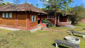 A rustic wooden cabin with a tiled roof, a small porch, and a fire pit. - Jungle Mount Adventures (Madikeri)