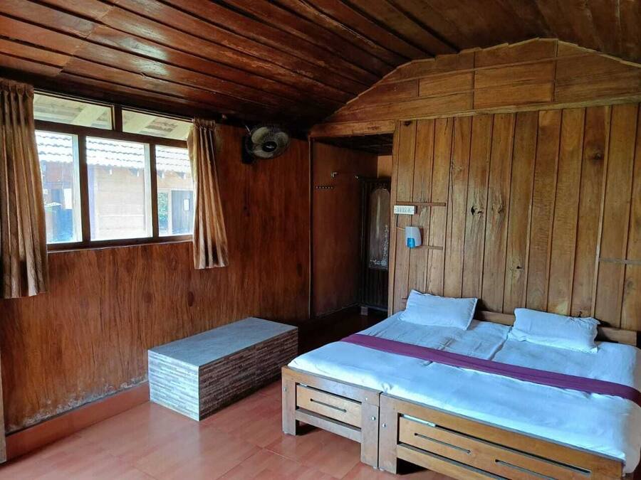 Une chambre dans une cabane en bois, avec un lit, un banc et une fenêtre avec des rideaux.