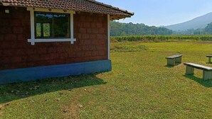 A small brick building with a tiled roof and a window. There are two concrete benches in the grassy area in front. - Jungle Mount Adventures (Madikeri)